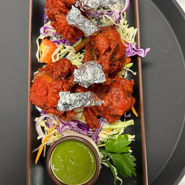 Red chicken lollipops with foil-wrapped bones, served on shredded cabbage and onions with green chutney.