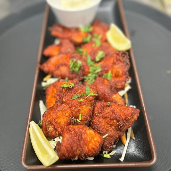 Spicy red chicken wings garnished with cilantro and lemon wedges on a dark rectangular plate.