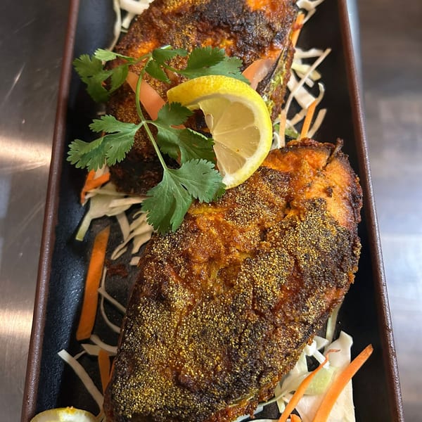 Two pieces of fried fish, garnished with cilantro and a lemon wedge, on a bed of shredded cabbage.