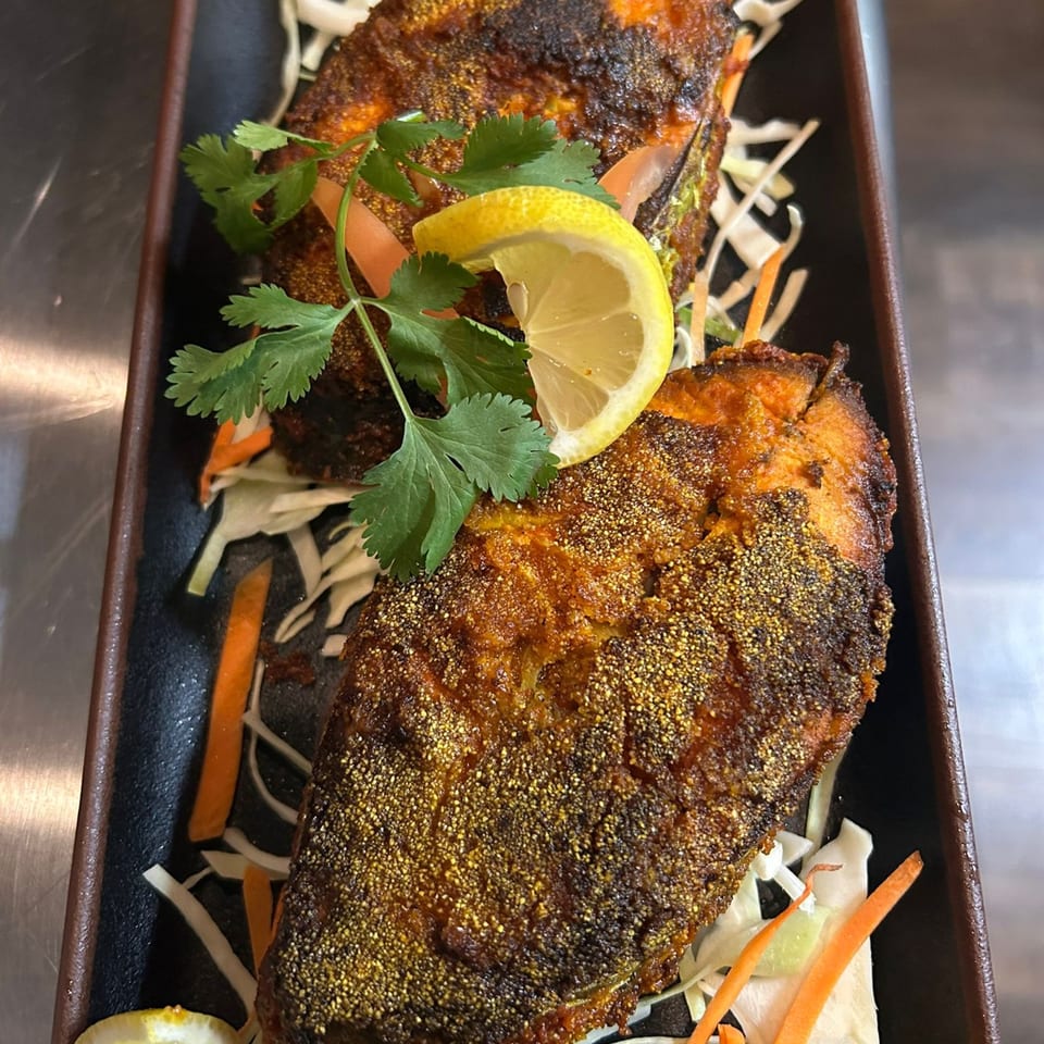 Two pieces of fried fish, garnished with cilantro and a lemon wedge, on a bed of shredded cabbage.