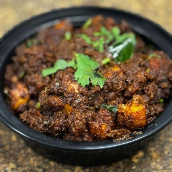 Close-up of a dark, rich Indian curry dish with paneer and fresh cilantro in a black bowl.