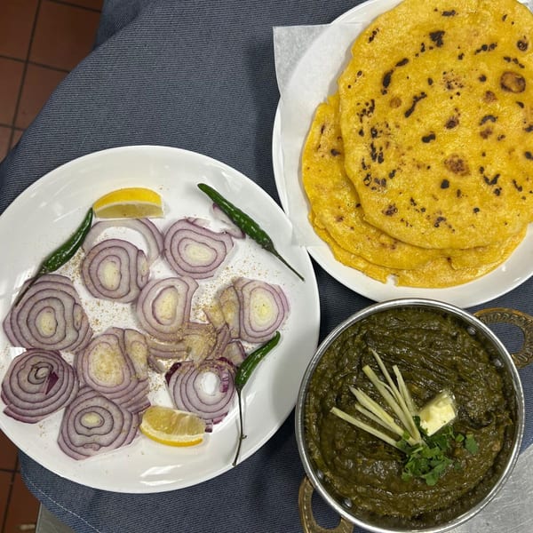 Indian dish of saag, makki di roti, and sliced red onions with lemon and green chilies.