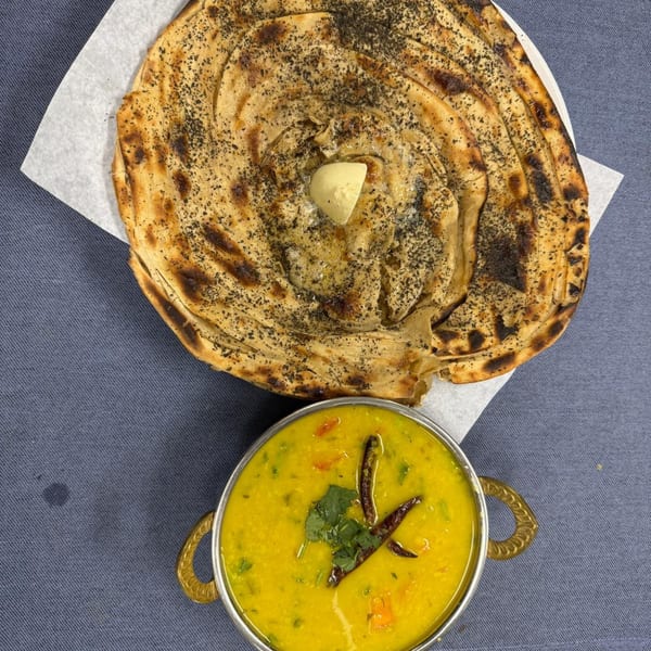 A golden-brown Indian paratha with butter and a bowl of yellow dal with spices.
