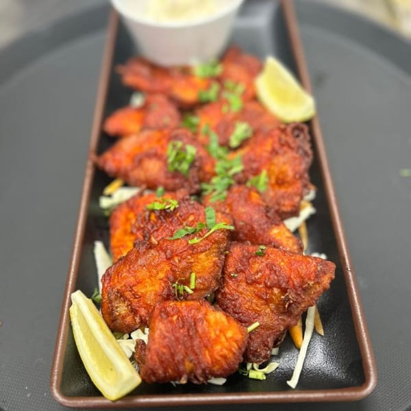 Spice Kitchen's Indian-style chicken wings, garnished with cilantro and lemon wedges, on a dark platter.