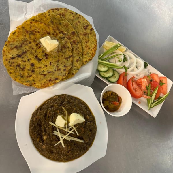 Indian meal with Makki ki Roti, Sarson ka Saag, and a side salad with pickles.